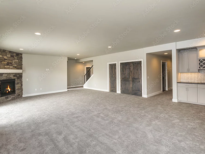 Empty renovated basement with fireplace and gray carpet